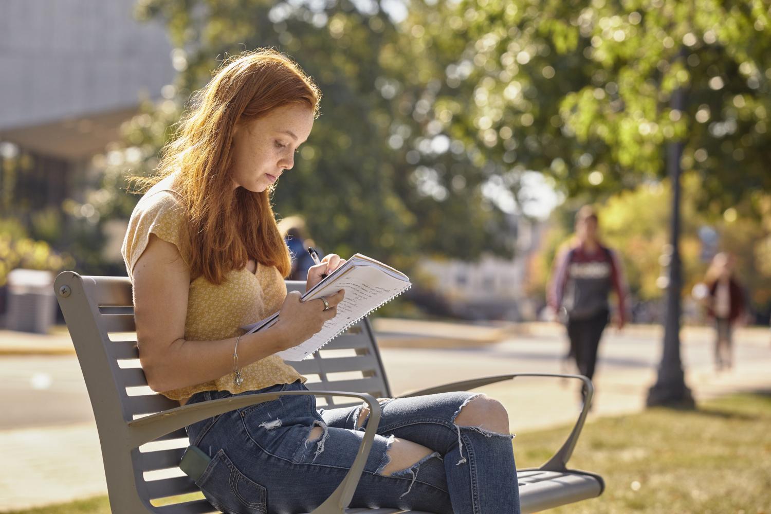 A <a href='http://l5dd7.regutilities.com'>BETVLCTOR伟德登录</a> student reads on a bench along Campus Drive.